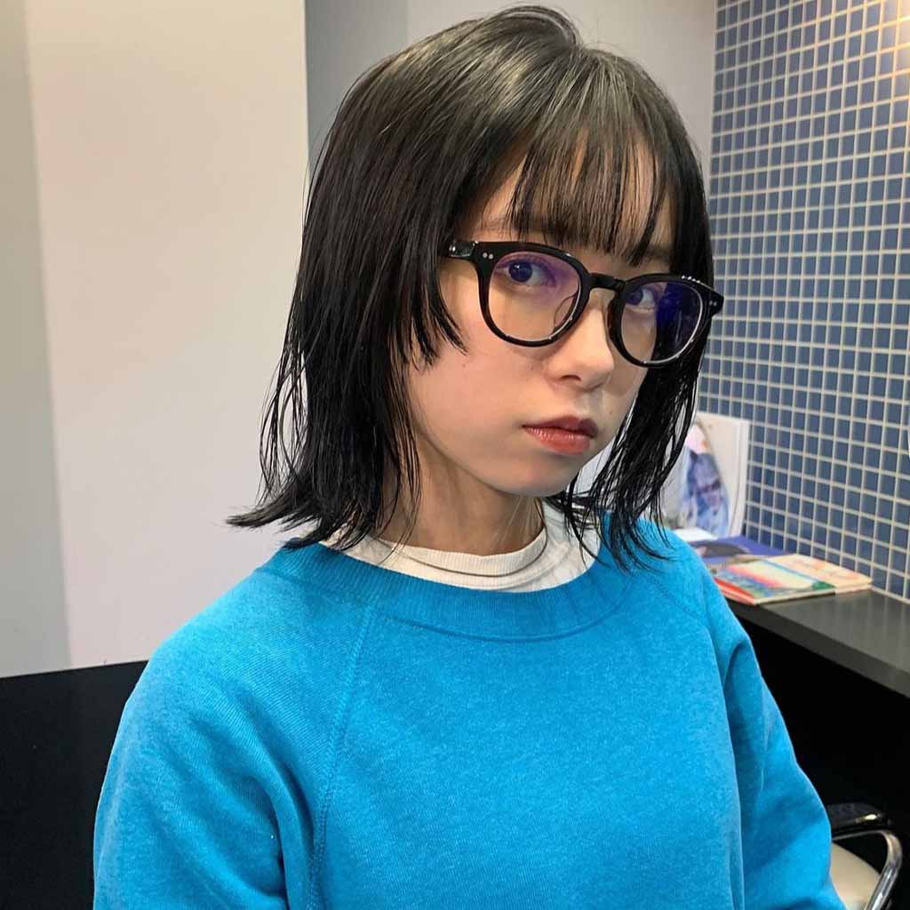 a girl with a bob wolf cut, wearing glasses and a blue sweater