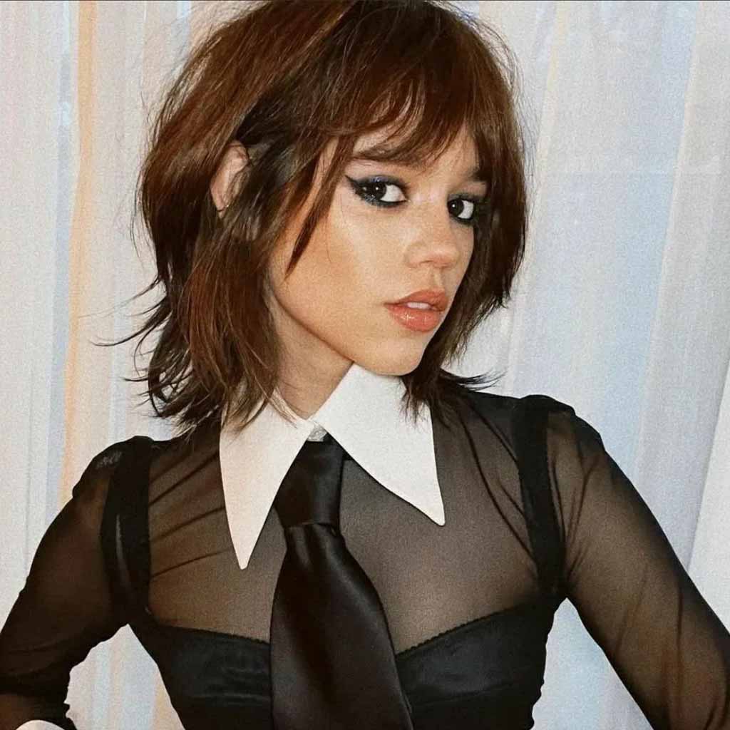 Jenna Ortega with a shaggy bob wolf cut wearing a net top