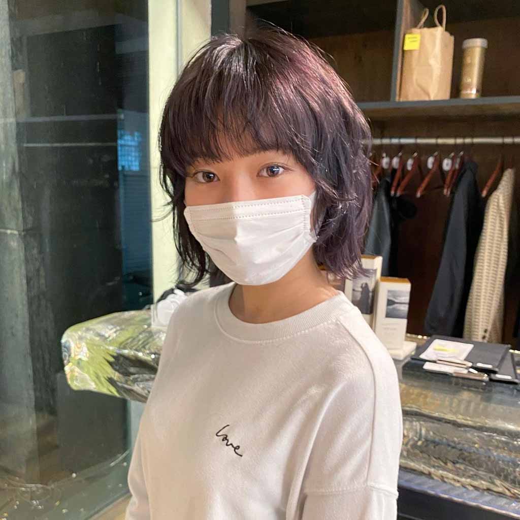 a girl with a bob wolf cut with bangs, wearing a mask and a white sweatshirt