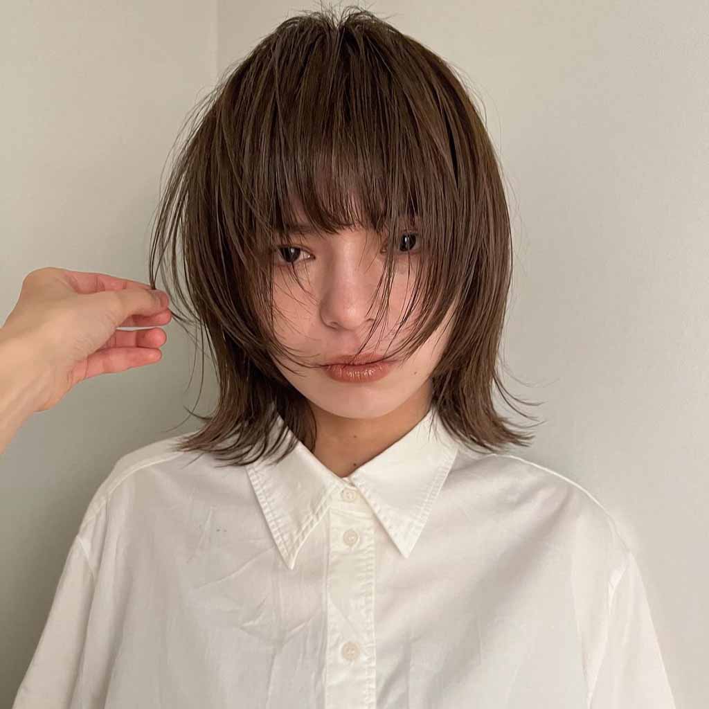 a girl with choppy bob wolf cut with long bangs, wearing a white shirt